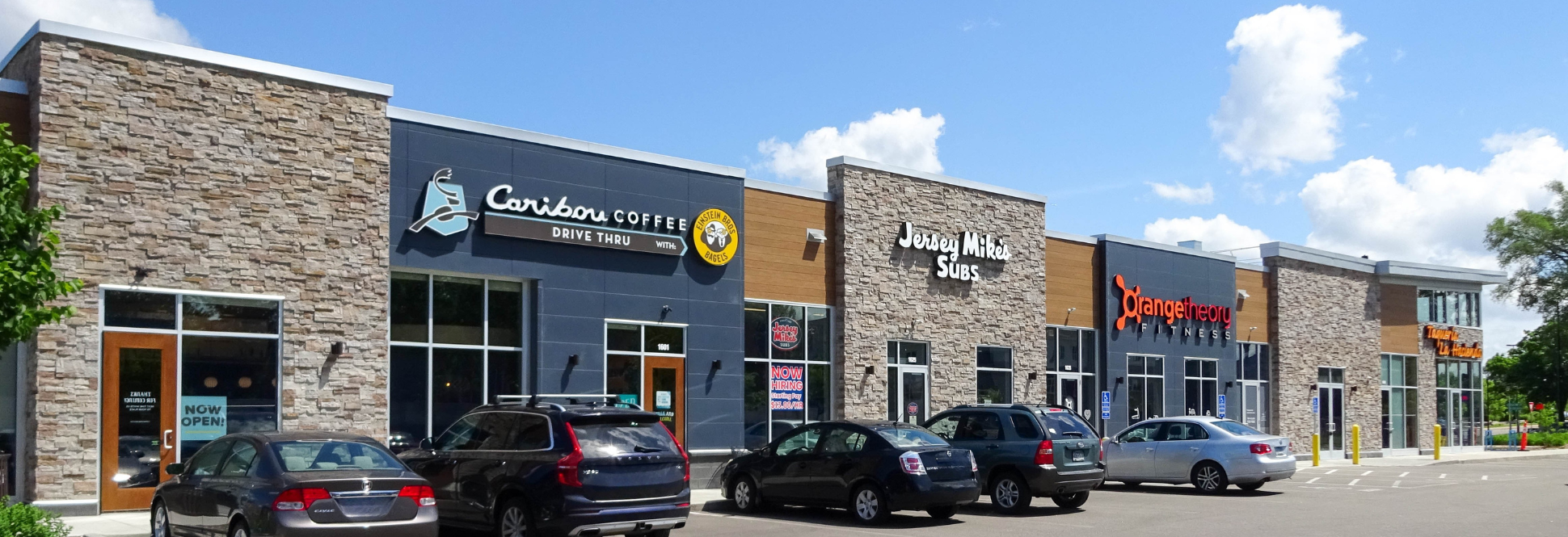 Modern multi-tenant retail center with stone and metal façade, storefront parking, and pedestrian-friendly site layout.